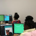 Adult stands in front of multiple young people at computers in classroom setting.